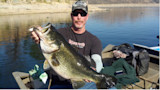 Man in sunglasses holding a large bass in a boat on a calm lake