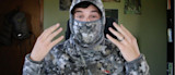 Man in digital-camo balaclava and cap, hands raised showing ring