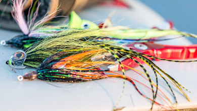 Colorful long streamer fishing lures with a pair of red fishing pliers on a boat deck