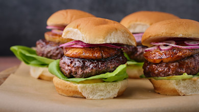 Pineapple-topped beef sliders with lettuce and sliced red onion on soft buns