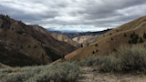 Dry rolling hills and sagebrush in a rugged valley beneath heavy gray clouds