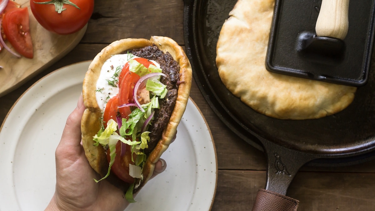 Venison gyro in pita with smashed patty, tomato, red onion, lettuce and yogurt sauce; cast-iron skillet with pita