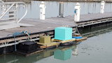 Turquoise box and two crates floating on tire pontoons beside a wooden marina dock