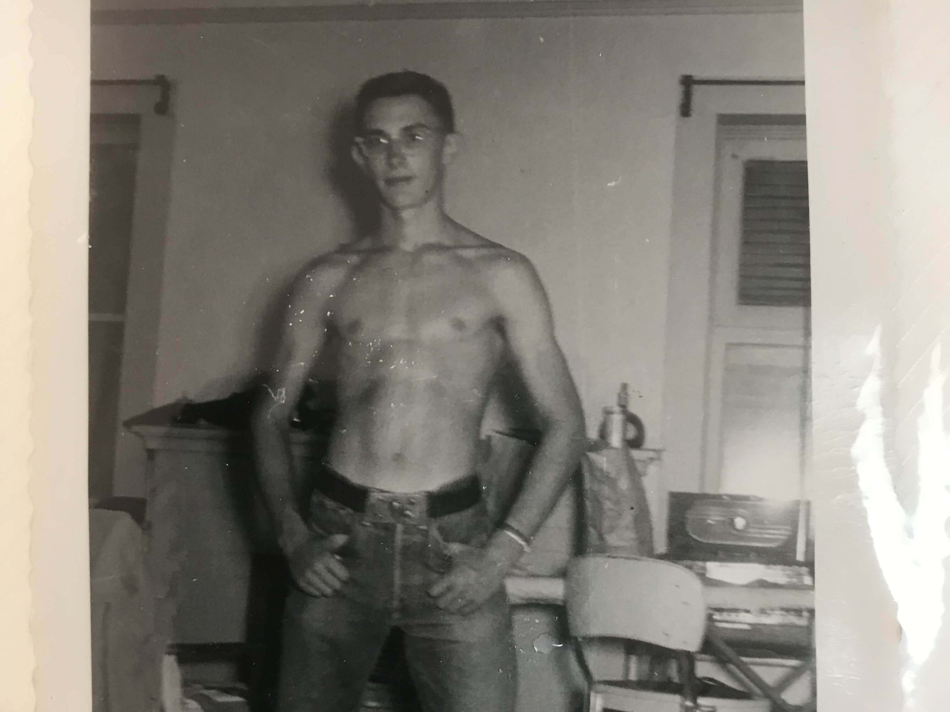 Shirtless young man in glasses and jeans standing with hands on hips in a room