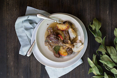 Apple-braised hog with apple slices and torn bread in broth, served in a bowl on a napkin.