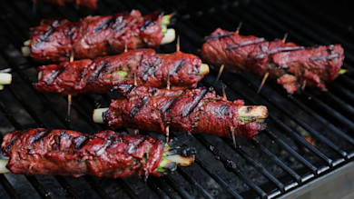 Grilled venison negimaki rolls wrapped around scallions, skewered with toothpicks and charred on grill grate