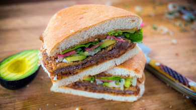 Halved torta sandwich stacked with avocado, pickled onions and greens on a wooden board