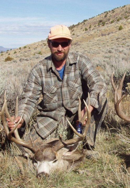 Hunter kneeling behind a deer, holding its antlers, wearing orange cap and sunglasses