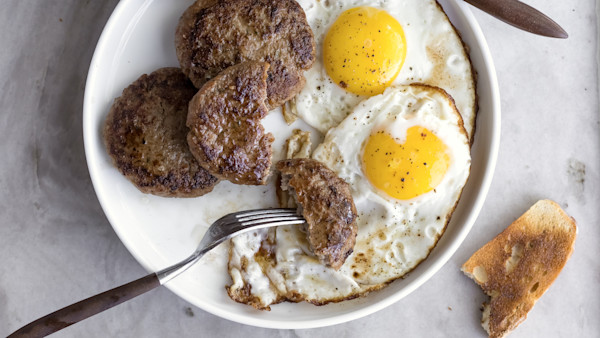 Bowl with two fried eggs, four browned breakfast sausage patties and a piece of toast