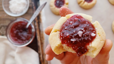 Hand holding bitten thumbprint cookie topped with rosehip jam and coarse salt