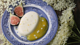 Creamy panna cotta with elderflower blossoms, fig halves, and yellow sauce on blue patterned plate