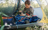 Man packing camp stove inside mesh tent on blue NEMO sleeping bag
