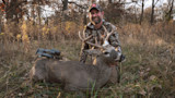 Hunter kneeling behind a harvested whitetail buck, holding its antlers