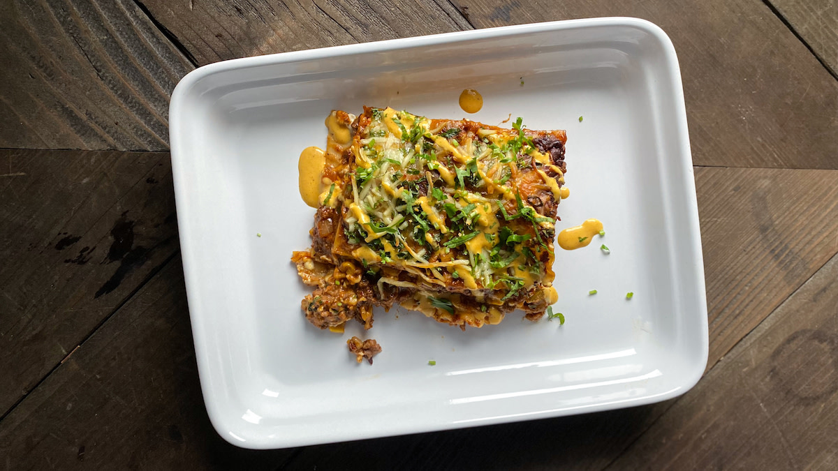 Enchilada-lasagna square topped with melted cheese, chopped herbs and orange sauce on white plate