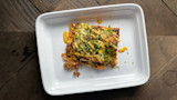 Enchilada-lasagna square topped with melted cheese, chopped herbs and orange sauce on white plate