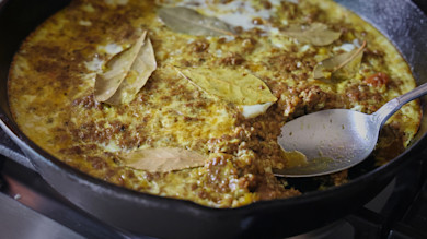 Venison bobotie in cast-iron skillet topped with bay leaves and a spoon