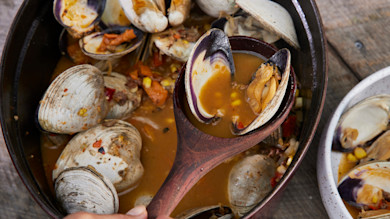 Steamed clams and smoked garlic sausage in broth with corn and peppers, wooden spoon