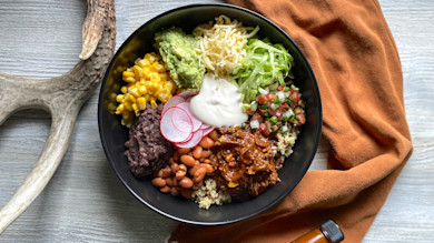 Burrito bowl with shredded barbecue meat, quinoa, pinto & black beans, corn, guacamole, lettuce, radish, sour cream