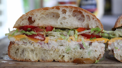 Ciabatta sandwich cut in half with tuna salad, cheddar, tomato, shredded lettuce