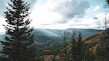 Mountain valley with evergreen trees and layered ridges under a cloudy sky