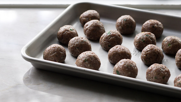 Raw seasoned meatballs neatly arranged on a metal baking sheet