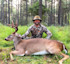 Hunter kneeling behind large buck with antlers in a pine forest