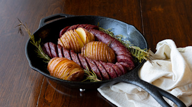 Sliced sausage and hasselback potatoes in cast-iron skillet with rosemary