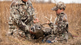 Boy kneeling with adult holding a harvested buck's antlers in tall grass