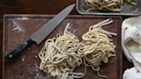 Fresh homemade ramen noodles on wooden cutting board with chef's knife and towel