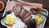 Sliced smoked venison roast on tray with potato salad, pickles, onions and BBQ sauce