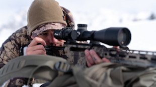Hunter aiming camouflaged rifle with scope in snowy field