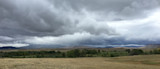 Dark storm clouds over distant mountains, rolling grassland and a tree line