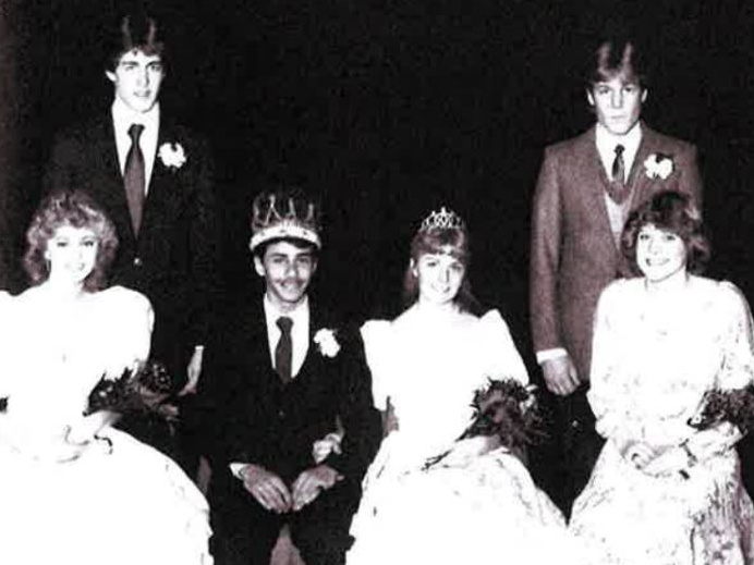 Black-and-white group portrait of three crowned people seated in gowns with three people in suits standing behind