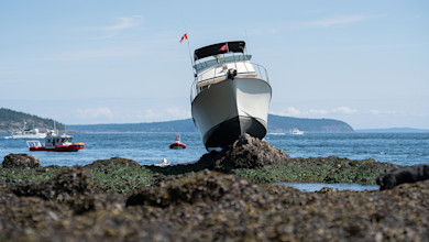 Motorboat grounded on rocky shore at low tide with Canadian flag, rescue boats nearby
