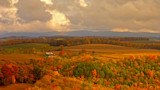 Autumn farmland with colorful trees, rolling cornfields, small red barn under cloudy sky