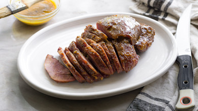 Smoked ham glazed in honey-mustard, sliced on white oval plate with knife and glaze brush
