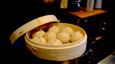 Nine steamed soup dumplings in a partially open bamboo steamer