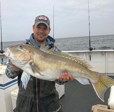 Fisherman holding large yellow-striped fish on a boat deck, ocean in background