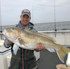 Fisherman holding large yellow-striped fish on a boat deck, ocean in background