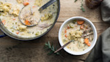 Creamy herbed-dumpling soup with shredded meat, carrots and celery in pot and bowl on wood