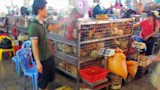 Live chickens in stacked wire cages at a crowded indoor market, vendors nearby