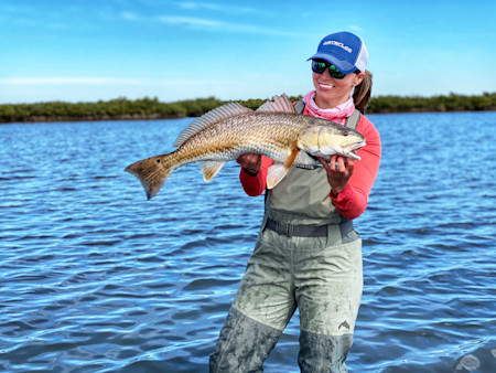 Woman holding large fish in shallow water, wearing blue cap reading WATERLOO
