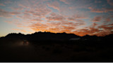 Pickup truck on dusty road at sunset, silhouetted mountain range and orange clouds