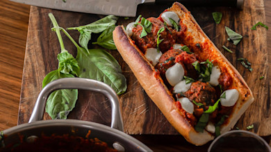 Meatball sub with tomato sauce, melted mozzarella and basil on wooden cutting board
