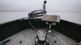 Boat bow with Ultrex trolling motor and rain‑spattered fishfinder on a foggy lake