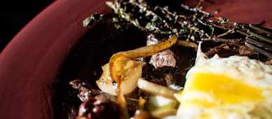 Steak bites with caramelized onions, herb sprig and runny fried egg on red plate