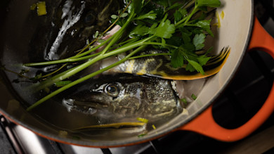 Two whole fish with parsley in simmering broth inside orange enameled pot