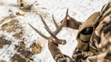 Hunter holding shed antler in gloved hands over snow