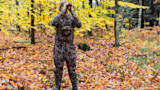 Hunter in camouflage using binoculars in forest of yellow autumn leaves