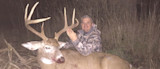 Hunter kneeling behind large buck with tall antlers in field at night